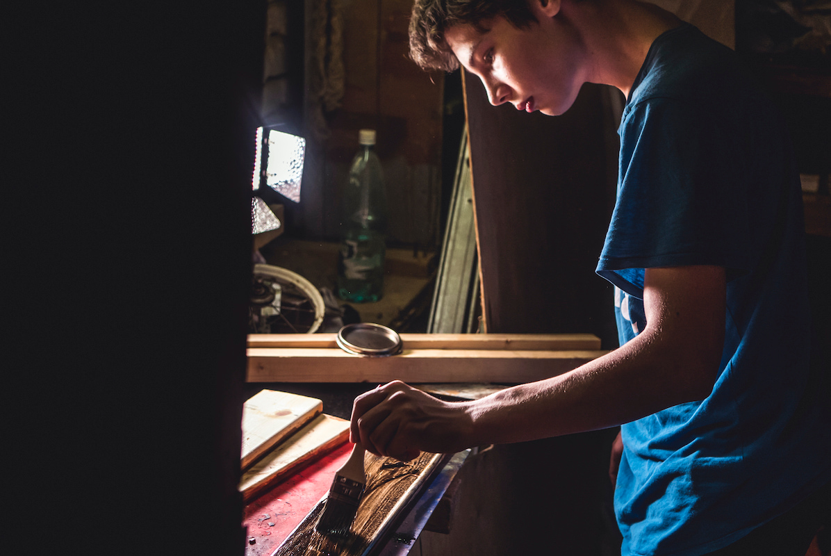 Junger Handwerker bearbeitet Holz mit Pinsel.