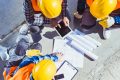 Drei Bauarbeiter mit Helmen besprechen Pläne